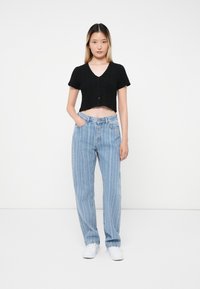 Haut noir, cropped, à manches courtes avec une finition texturée et un décolleté en V, associé à un jean taille haute rayé verticalement à rayures bleu clair. Chaussures blanches.