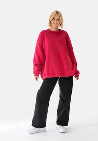 Czerwona, oversize'owa bluza z bawełny, z długimi rękawami i okrągłym dekoltem, w połączeniu z luźnymi czarnymi spodniami i białymi butami.