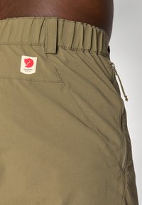 Denumire scurtă: pantaloni scurți de culoare verde măsliniu, confecționați dintr-o țesătură ușoară, cu un tiv elastic, buzunar lateral și eticheta brandului Fjällräven pe talie.