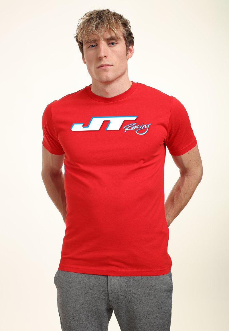 Rød kortærmet t-shirt lavet af bomuld med et blåt og hvidt "JT Racing" logo på forsiden. Glat tekstur, klassisk pasform.