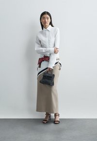 Camisa branca com botões, saia bege com detalhe padrão, mala preta e saltos pretos. Tecidos lisos com formas e detalhes definidos.