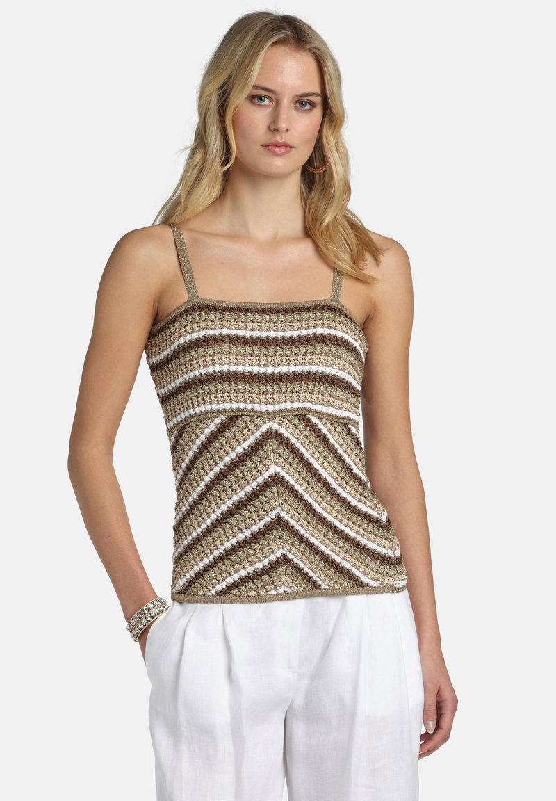 Mujer con un top de crochet sin mangas a rayas en beige, marrón y blanco, combinado con pantalones blancos y accesorios como pulseras y pendientes de aro.