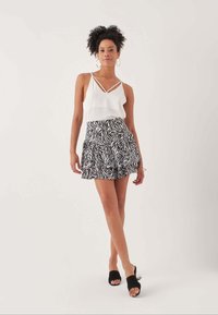 Top bianco senza maniche con spalline incrociate, abbinato a una gonna svasata con motivo zebratto in bianco e nero e sandali neri scivolati.
