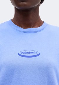 Άτομο που φοράει ένα ανοιχτό μπλε t-shirt Patagonia με στρογγυλή λαιμόκοψη και το λογότυπο της μάρκας τυπωμένο σε πιο σκούρο μπλε στο στήθος.