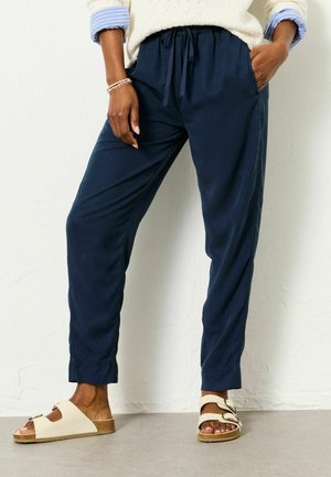 Navy blue, lightweight pants with an elastic waistband and side pockets, paired with beige sandals featuring adjustable straps and cork soles.