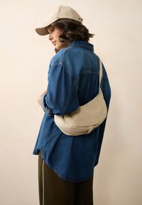 Zils džinsa krekls apvienots ar olīvu zaļām biksēm, ar bēša krāsas plecu somu ar teksturētu virsmu un izliekta forma.