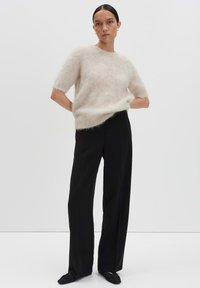 Pull en beige clair pelucheux à manches courtes, associé à un pantalon large noir. La tenue présente une coupe décontractée et des textures douces.