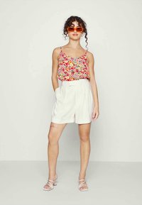 Top de alças com padrão floral em vermelho, rosa e amarelo. Calções brancos de cintura alta com bolsos. Modelo a usar óculos de sol laranja e sandálias com tiras.