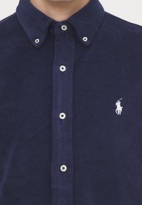 Mörkblå knappad skjorta i mjuk frotté med klassisk krage, med vita knappar och en liten broderad logotyp på bröstet.