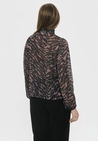 Blusa negra transparente con un patrón abstracto en rosa y marrón, cuello alto y puños elásticos. Tejido ligero y texturizado con pliegues sutiles.