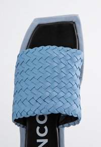 Niebieska pleciona skórzana sandałka wsuwana ze kwadratowym noskiem, gładką czarną wkładką i jasnoniebieskim zamszowym obcasem. Posiada teksturowany wzór na cholewce.