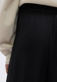 Μαύρη, υφασμάτινη φούστα με ελαστική μέση, εμφανιζόμενη δίπλα σε ένα λευκό φούτερ. Το ύφασμα φαίνεται αέρινο και απαλό.