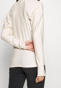 Cremfarbener Langarm-Top mit gerafftem Texturdetail auf der Rückseite, slim fit und weichem Stoff. Kombiniert mit dunkel (-en) enganliegenden Hosen.