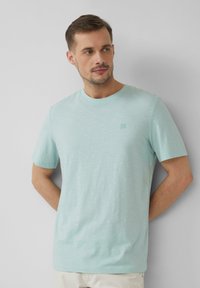 Jasnoniebieska koszulka z krótkim rękawem, z okrągłym dekoltem i subtelnym logo na klatce piersiowej, wykonana z miękkiego, teksturowanego materiału.