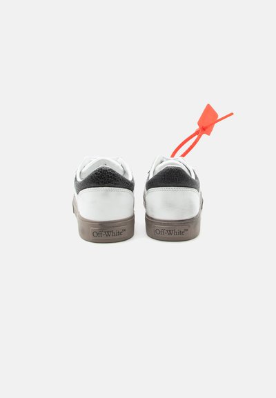 Ζευγάρι παπουτσιών Off-White, λευκά και μαύρα, εμφανιζόμενα από πίσω, με καφέ σόλες και φωτεινή πορτοκαλί ετικέτα φερμουάρ στο δεξί παπούτσι.