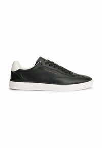 Baskets basses noires avec semelle blanche et talon, lacets noirs, et petit logo doré "Tommy Hilfiger" sur le côté.