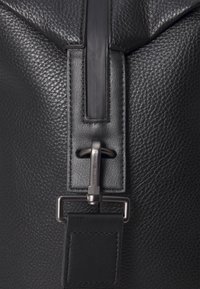 Sac en cuir noir avec une surface texturée, une fermeture éclair noire lisse et un détail de fermeture métallique. Éléments de design simples et fonctionnels.