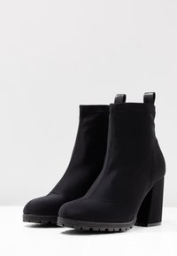 Bottines noires en tissu extensible avec un talon épais, bout rond et languettes en haut, dotées d'une semelle texturée pour une bonne adhérence.