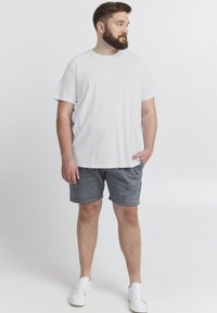 Hvit bomullst-skjorte med korte ermer, kombinert med grå teksturerte shorts. Modell iført hvite joggesko, stående mot en ensfarget bakgrunn.