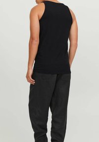 Black sleeveless tank top made of soft cotton, featuring a classic fit and rounded neckline, paired with dark pants.