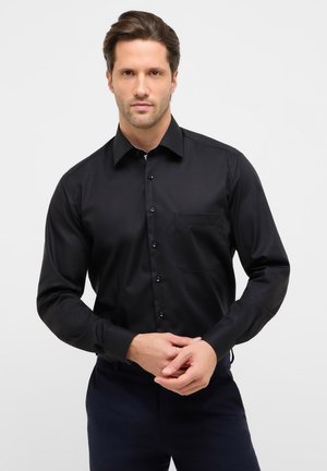 Schwarzes langärmeliges Hemd aus glattem Stoff mit spitzem Kragen, Knopfleiste vorne und einer Brusttasche. Die Passform ist tailliert, und die Manschetten sind mit Knöpfen versehen.