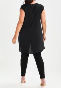 Černá, volná tunika s krátkými rukávy a zakřiveným lemem, kombinovaná s černými legínami. Hladká tkanina a mírný rozparek na zádech.