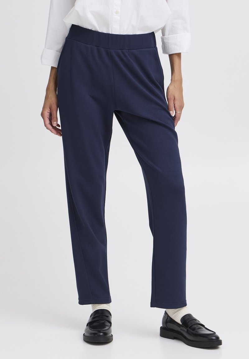Pantaloni blu navy con vita elasticizzata in un tessuto morbido, caratterizzati da una vestibilità comoda e gambe dritte, abbinati a mocassini neri e calzini bianchi.
