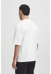Hvid bomulds t-shirt med korte ærmer og rund halsudskæring. Har en lige kant og en lille etiket på siden. Ingen synlige mønstre.