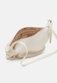 Cream soft leather crossbody bag with adjustable strap, zipper closure, and inner zippered pocket lined with branded fabric.