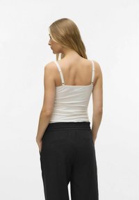 Top a canotta bianca aderente con spalline sottili, abbinato a pantaloni neri larghi con vita elastica e tasche laterali.
