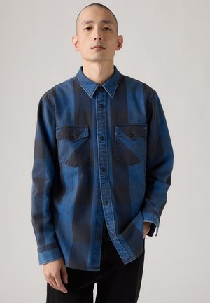 Camicia di jeans a quadri blu e nera con chiusura a bottoni, due tasche sul petto e colletto. Tessuto di peso medio con una trama liscia.