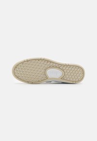 Vans sneakersåle med beige gummi, teksturert grep mønster og hvit merkevare. Har avrundede kanter og et klassisk vaffeldesign.