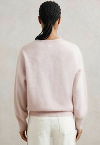 Maglione rosa chiaro e morbido con scollatura rotonda e maniche lunghe leggermente a sbuffo, abbinato a pantaloni bianchi. Texture soffice, vestibilità casual.