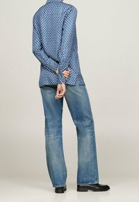 Sininen kuvioitu nappipaita, jossa on kaulus, yhdistettynä vaaleansinisiin leveälahkeisiin farkkuihin ja mustiin kenkiin. Paidassa on pieniä valkoisia ja punaisia kuvioita.