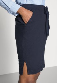 Námorně modrá bavlněná sukně se stahovacími šňůrkami v pase, bočními kapsami a rozparkem na lemu pro zvýšení stylu a usnadnění pohybu.
