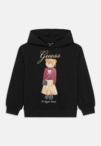 Hoodie noir avec un design d'un ours vêtu d'un haut rouge et d'une jupe plissée. Les accents comprennent le logo "Guess" en doré.