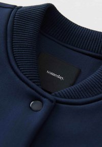 Marineblaue Sweatshirt mit geripptem Kragen und schwarzem Druckknopf. Das Etikett trägt die Aufschrift "irgendwann". Das Material wirkt glatt und strukturiert.