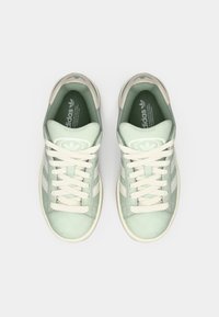 Light green sneakers made of suede, featuring white stripes, a rounded toe, and beige accents. Laces are evenly tied, logo visible on the tongue.
