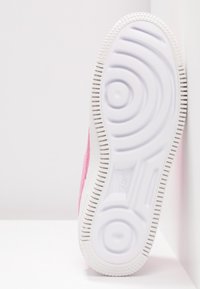 Semelle de basket blanche avec des motifs circulaires antidérapants et un bord texturé, présentée verticalement sur un fond clair uni.