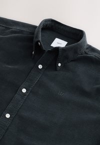 Czarna koszula zapinana na guziki o fakturze, z białymi guzikami i małym haftowanym logo korony na piersi, metka NEXT wewnątrz kołnierzyka.