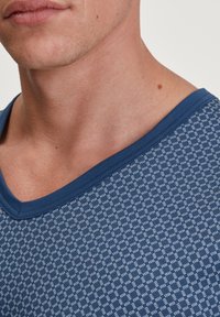 Marineblauwe T-shirt met een V-hals, voorzien van een gestructureerd patroon van kleine witte vierkanten en een zachte, gladde stof.