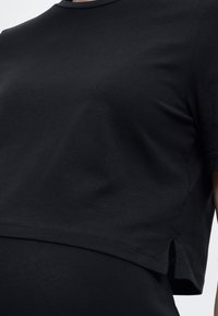 Κοντινό πλάνο ενός ατόμου που φοράει μια απλή μαύρη κοντή μπλούζα με πλαϊνές σχισμές και μαύρο παντελόνι με ψηλή μέση.