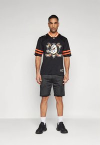 Musta jääkiekkopaita oransseilla yksityiskohdilla ja logolla, yhdistetty mustiin verkkoshortseihin ja mustiin lenkkareihin, joissa on rento malli ja urheilullinen muotoilu.