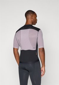 T-shirt de sport à manches courtes avec un design texturé noir et violet clair, doté de panneaux en maille et d'une poche zippée au dos.