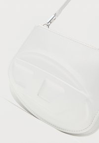 Λευκή τσάντα χειρός από συνθετικό δέρμα με ομαλή υφή, καμπυλωτό σχέδιο και ανάγλυφες λεπτομέρειες. Διαθέτει ασημένιες μεταλλικές συνδέσεις για το λουράκι.