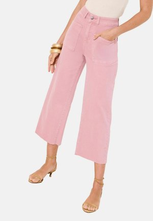 Naine kannab kõrge vöökohaga, laiade jalgadega roosasid lühendatud pükse suurte esitammetega, beežid rihmikud kontsadel, kuldseid käevõrusid ja valget topi.