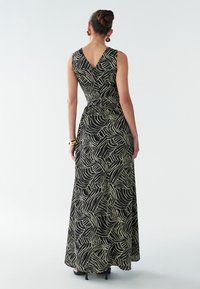 Vestido largo negro con escote en V en la espalda, con un patrón de líneas blancas onduladas. La tela es suave y llega casi hasta el suelo, con una cintura ajustada.