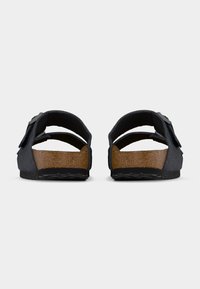 Ζευγάρι μαύρα σανδάλια με ανοιχτή μύτη και καφέ πάτους από φελλό, ρυθμιζόμενα λουράκια και ανάγλυφες μαύρες σόλες, που φαίνονται από πίσω σε απλό φόντο.