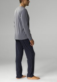 Szara koszula z długim rękawem połączona z granatowymi spodniami od piżamy w małe, białe owalne kształty. Miękka tkanina, luźny krój.