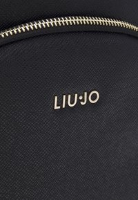 Zaino in pelle nera texture con una zip dorata prominente e il logo "LIU·JO" in lettere dorate sul davanti.